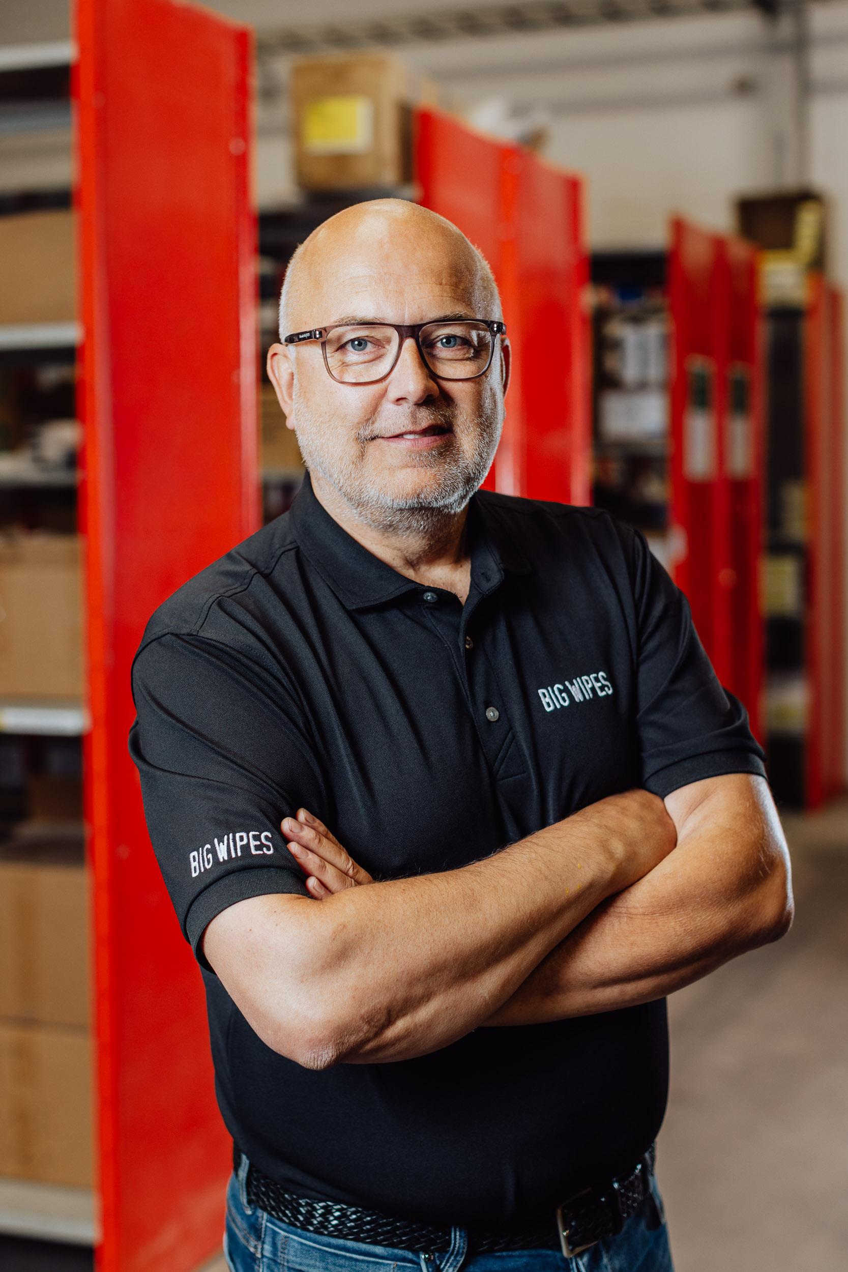 Ulf Carlson ler mot kameran, med armarna i kors, i bakgrunden syns en blurrad lagerlokal.