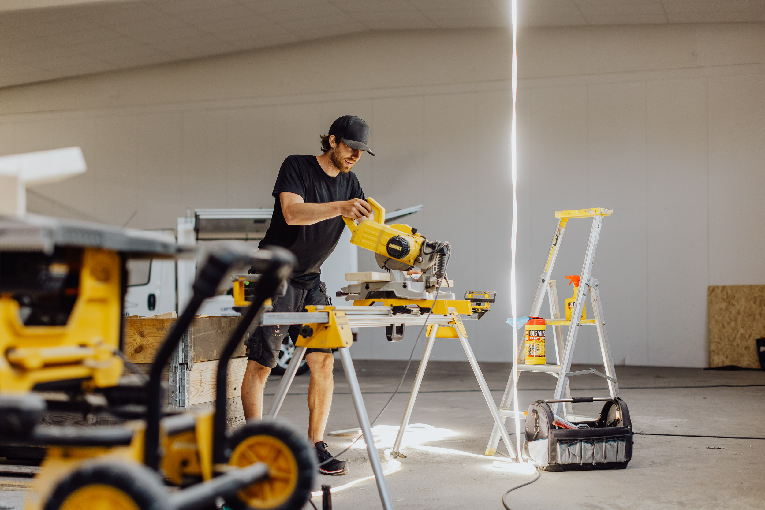 Hantverkare som sågar i industrilokal med byggprodukter. Produkterna Heavy Duty och Power Spray syns i bakgrunden.