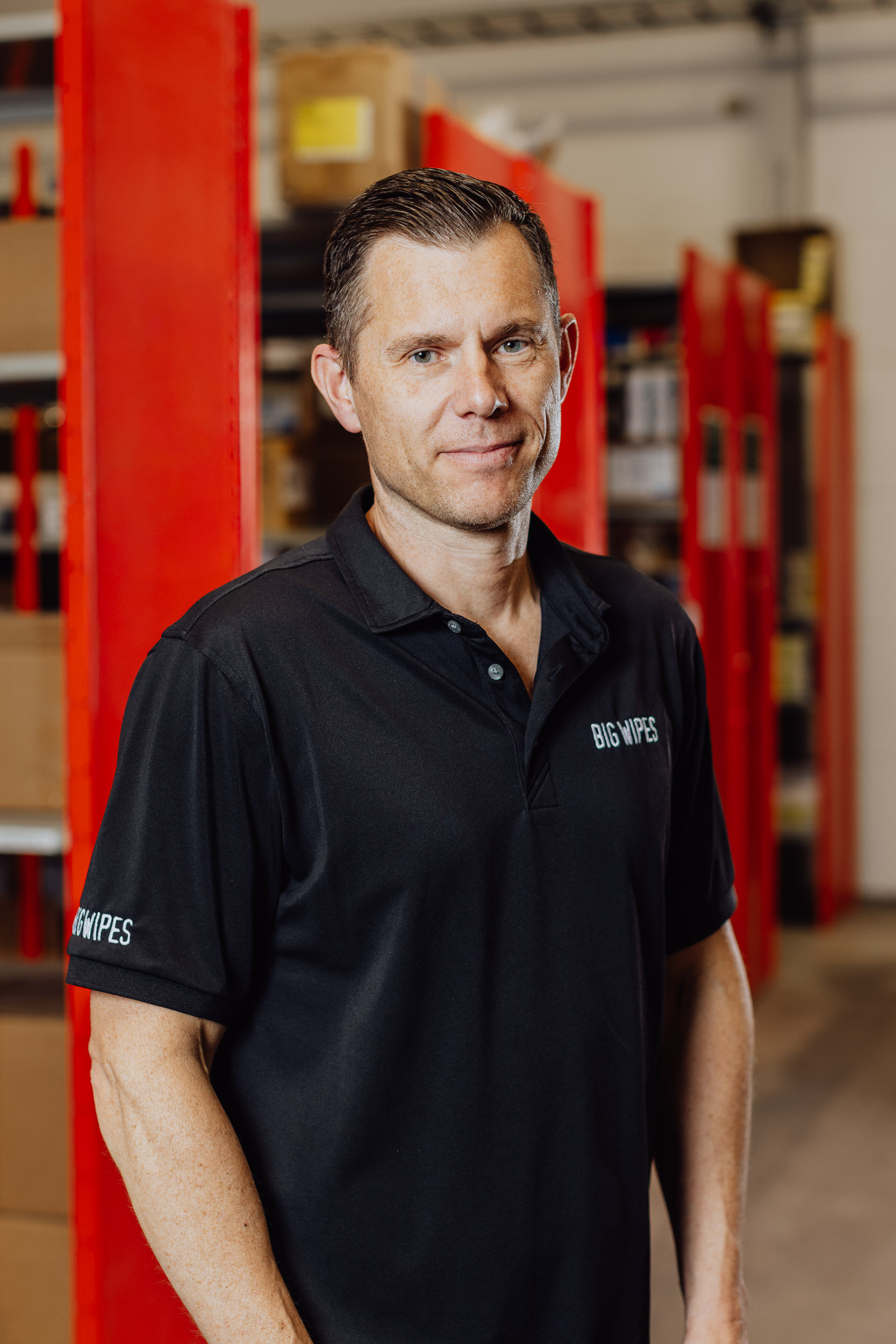 Linus Nilsson ler mot kameran, med armarna hängandes längs med sidan av kroppen, i bakgrunden syns en blurrad lagerlokal.