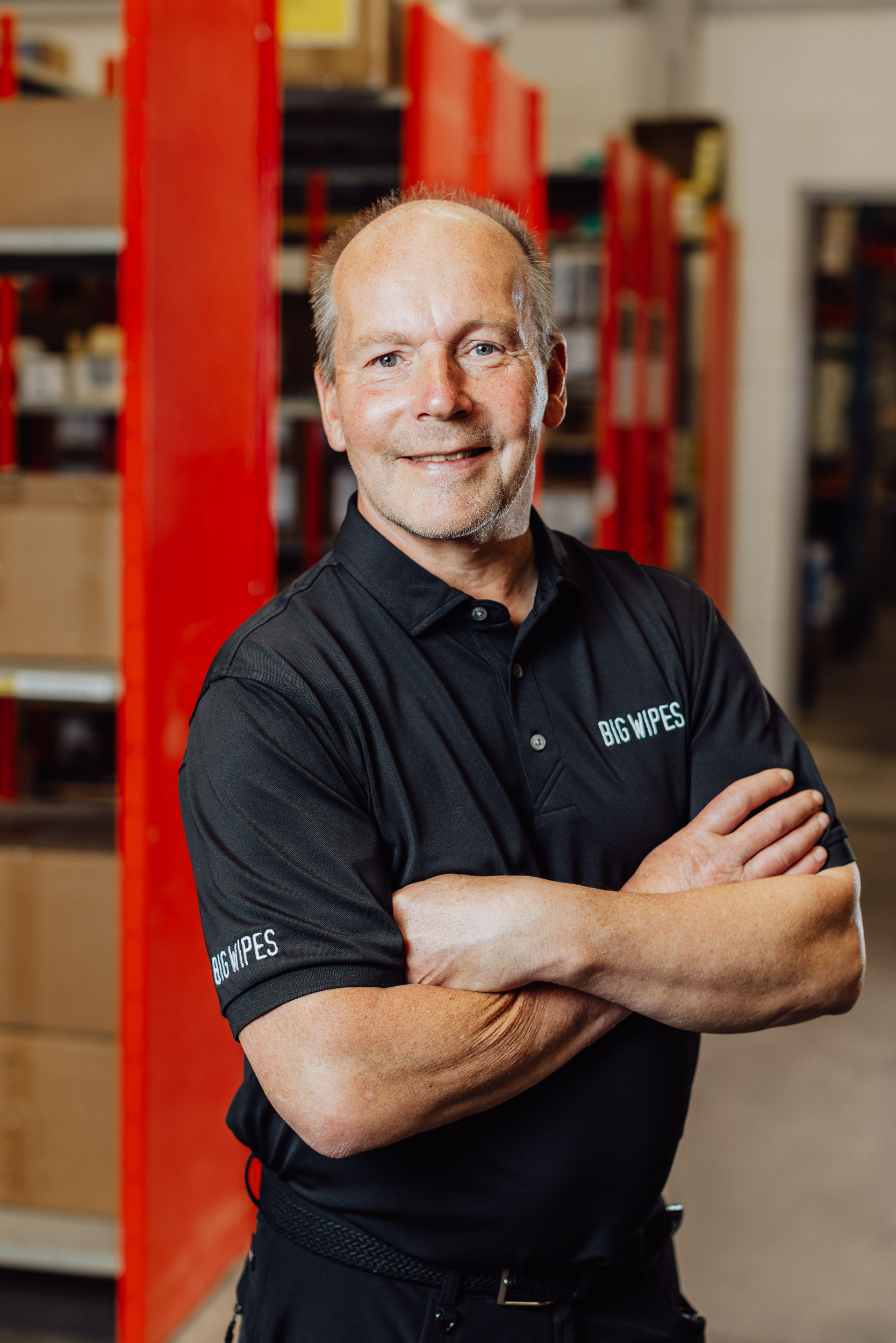 Patrik Johansson ler mot kameran, med armarna i kors, i bakgrunden syns en blurrad lagerlokal.