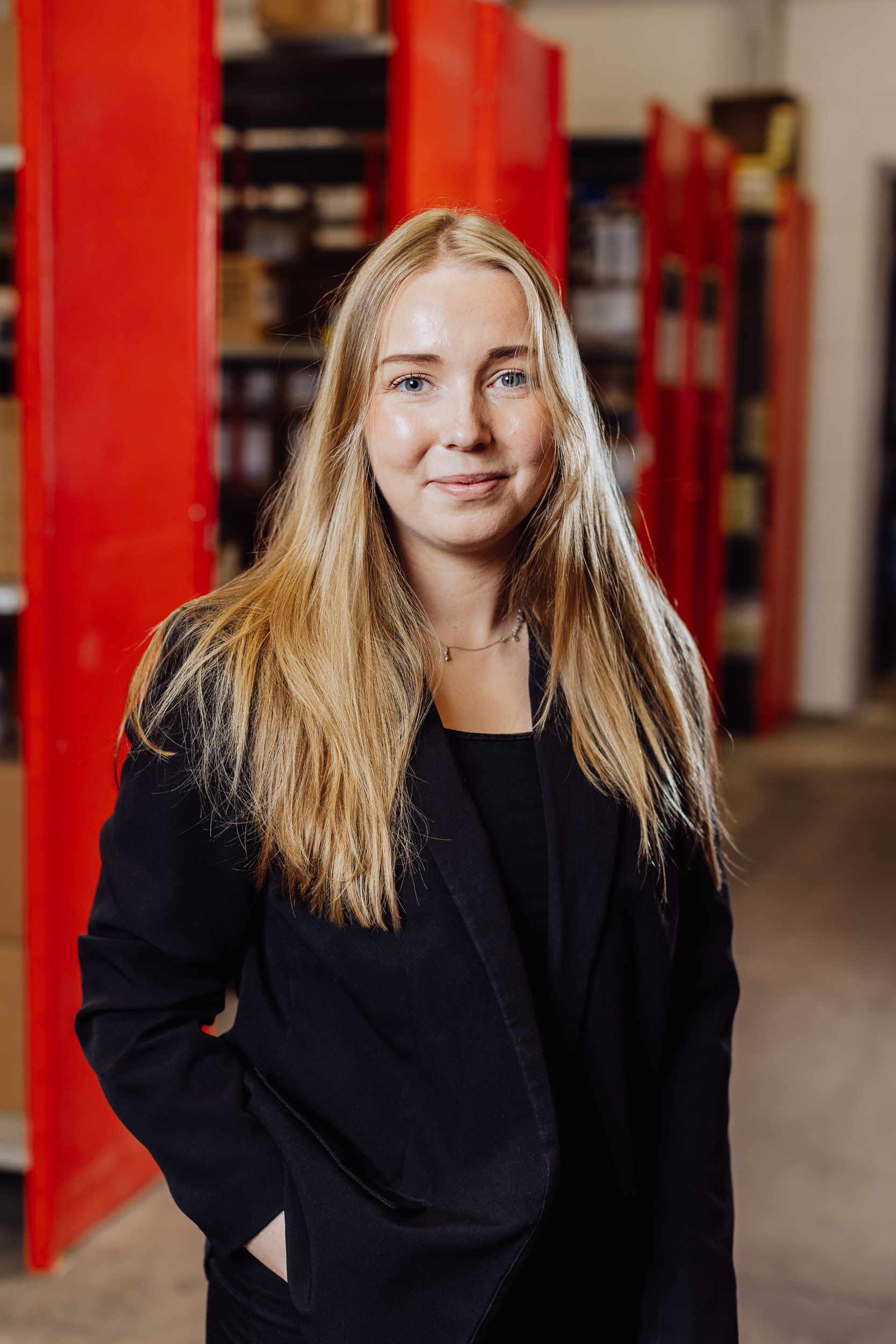 Sandra Johansson ler mot kameran, med ena armarna i midjan, i bakgrunden syns en blurrad lagerlokal.